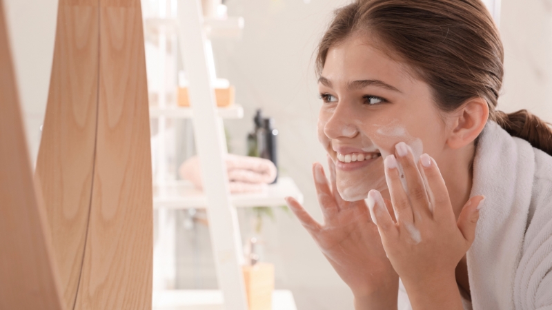 Tinejdžerka čisti lice penastom umivalicom ispred ogledala
