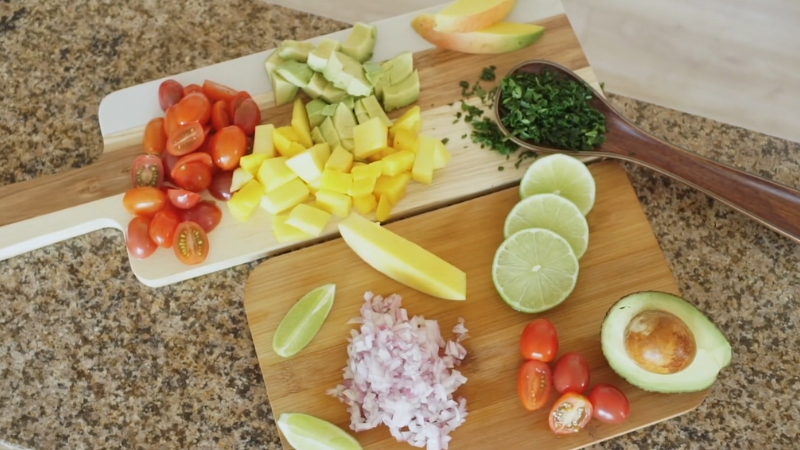 Sveže isečeno povrće i voće na dasci za sečenje, uključujući avokado, paradajz, mango, limetu i crveni luk
