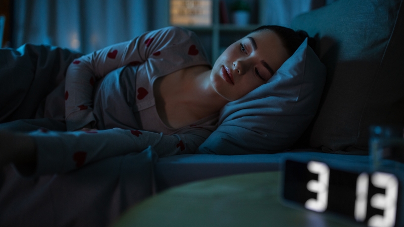 Tinejdžerka leži budna u krevetu noću dok sat pokazuje kasne sate